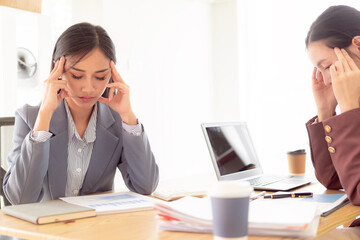 Asian woman pressing 2 hands on forehead feeling stressed, worried about bad financial business with documents and laptop on table