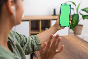 Woman in earphones talks on video call via mobile phone closeup young female waves hand in greeting lady communicates with friend remotely side view