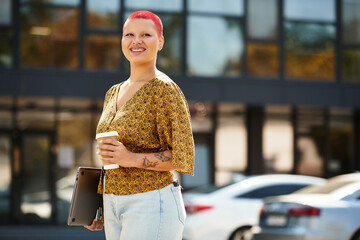 Wall Mural - A bald woman with a joyful smile holds a coffee cup while standing near a modern building.