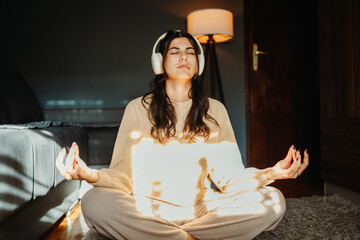 Young caucasian woman meditating with wireless headphones at home	
