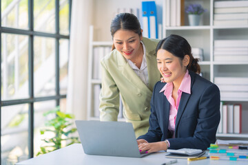 Two Asian businesswomen are deeply engaged in a discussion about data analysis work on a computer screen with graphs and charts. Showcase teamwork