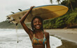 © lmot11 - African woman standing with surfboard on head on ocean beach. Black female surfer posing with surf board. Pretty multiethnic girl goes on surfing session on tropical location
