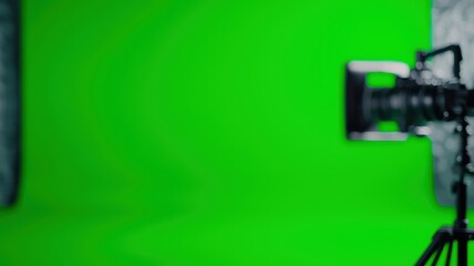 A professional camera on a tripod in front of a bright green screen backdrop, commonly used for chroma key video production.