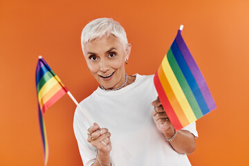 A stylish woman joyfully waves rainbow flags in a colorful setting.