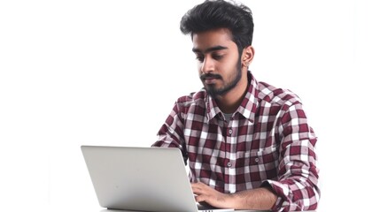 Man is sitting at a table with a laptop in front of him. He is wearing a red plaid shirt and he is focused on his work