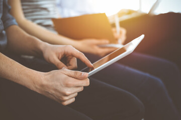 Wall Mural - Group of casual dressed business people working at meeting or conference in sunny office, close-up of hands. Businessman using tablet computer