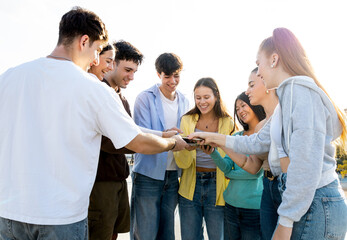 A group of 8 young people of different ethnicities between 18 and 25 years old have fun in the street at sunset.Millennials are passing files or connecting their phones.Concept of youth groups.