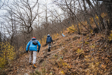 Two individuals are making their way up a steep hill nestled within the serene woods, enjoying the beauty of nature around them as they embark on this outdoor adventure together