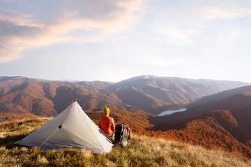 Wall Mural - Tourist near his tent against the backdrop of an incredible mountains landscape with lake on background. Sunny day in autumn highland