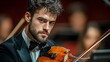 © Ratchadaporn - Close up portrait of a skilled male musician in a black tuxedo with a blurred stage backdrop behind him  The performer is intently focused on playing his violin
