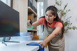 ©  NCST Studio - Asian woman cleaning office desk with disinfectant spray and blue cloth, wearing apron and gloves