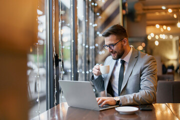 A mid adult Caucasian male executive sips coffee while attentively working on a laptop in a stylish, well-lit city cafe.