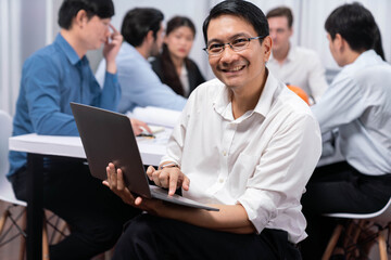 Confidence and happy smiling businessman portrait with background of his colleague and business team working in office. Office worker teamwork and positive workplace concept. Prudent