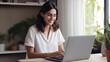 © Iona - Smiling young woman working remotely in a bright room, surrounded by plants, embodying a sense of positivity and productivity.