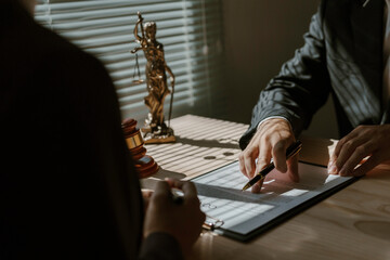 Lawyer pointing at contract details with pen, explaining agreement terms to client during office meeting, with gavel and themis statue