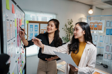 Two female web designers are discussing and analyzing mobile user interface ux ui design on whiteboard with sketches