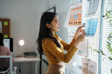 Asian female web designer arranging mobile application wireframes on a window in the office