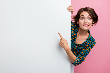 Poster - Portrait of impressed woman wear print blouse indicating at promo on white wall empty space biting lips isolated on pink color background