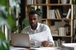 © useful pictures - Focused serious African American businessman analyzing documents while working at a desk in a modern office environment