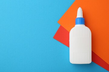 Wall Mural - Bottle of glue and colorful paper on light blue background, top view. Space for text