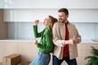 © DimaBerlin - Happy couple enjoy on moving day playful dancing with cardboard boxes, smiling in new kitchen. Filled with anticipation for future in new home man, woman celebrate joint purchase apartment in mortgage