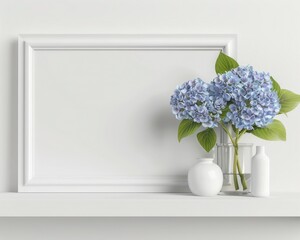 A white frame sits on a white shelf with blue hydrangeas in a vase and two white decorative items