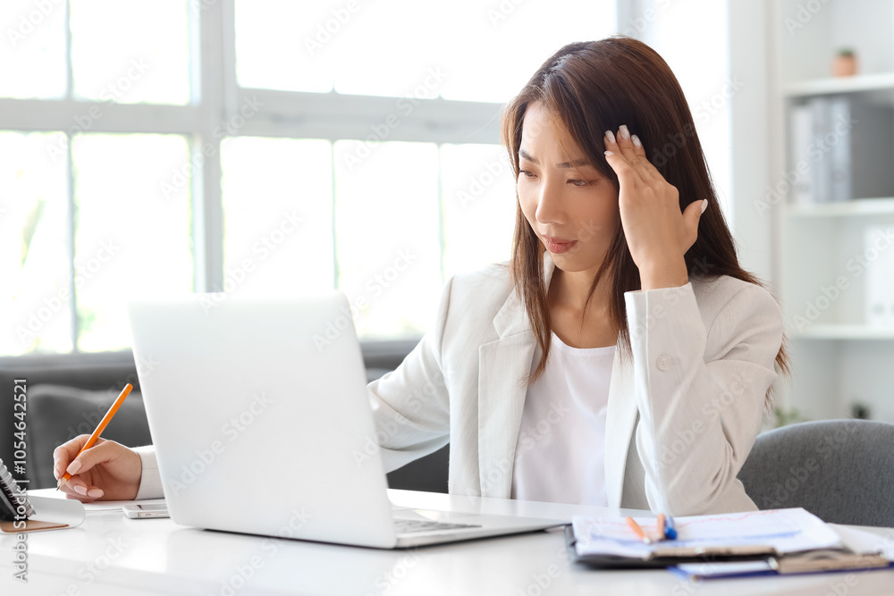 Tired Asian businesswoman working at table in office