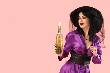 Beautiful young woman dressed as witch for Halloween with burning candle in bottle on pink background