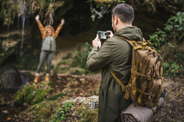 husband take a photo of wife backpacker in front cave in the forest