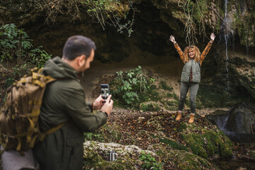 husband take a photo of wife backpacker in front cave in the forest