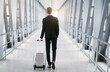 © Prostock-studio - Business Trip Concept. Back view of classy guy in suit pulling trolley bag walking out the airport, free space