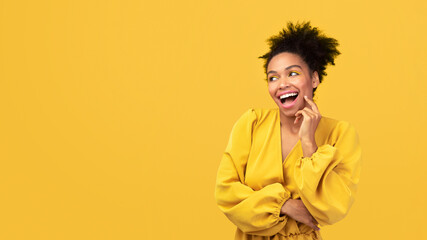 Wall Mural - Flirting Girl. Romantic afro woman in yellow dress touching cheek with finger isolated over pink studio wall, copyspace