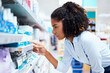 © peopleimages.com - Woman, search and reading with medicine at pharmacy for OTC pills, label and decision by shelf. Healthcare, drugstore and female customer with info on box for medical product, choice and supplements