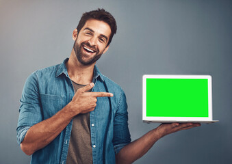 Poster - Happy man, tablet and pointing to green screen for advertising against a grey studio background. Portrait of male person smiling and showing technology display, chromakey or mockup for advertisement