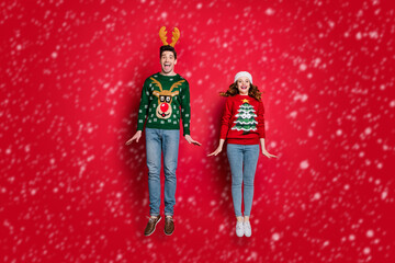 Full body photo of crazy lady and guy jumping high enjoy x-mas sale wear ugly ornament pullovers and headwear isolated red color background