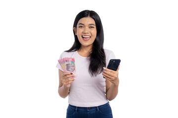 Happy young Asian woman holding Indonesian rupiah cash and smartphone, representing mobile banking or online payment on white background