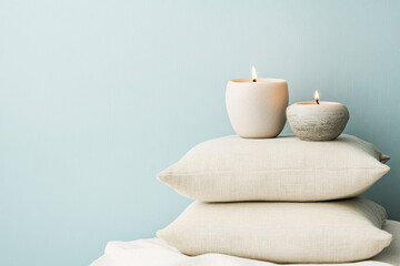 Cozy interior arrangement with soft pillows and lit candles on a light blue background