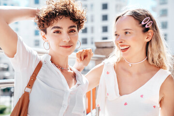 Two young beautiful smiling cute women in trendy summer sundress. Sexy carefree models posing in the street in sunny day. Positive models having fun and hugging. Cheerful and happy