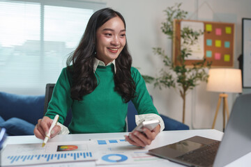 Asian office worker, businesswoman working in home office using laptop and mobile phone to do online business work in finance, marketing, accounting, contacting customers of the company.