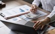 © wichayada - Young Businesswoman Analyzing Financial Documents and Data at Modern Office Desk with Laptop and Calculator
