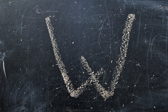 On an old school board, the letter W is written in white chalk.