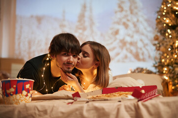 With decorated fir tree. Beautiful young couple indoors, celebrating new year against projector