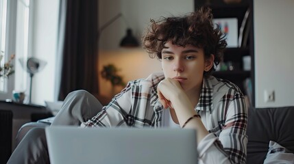 Non binary person using laptop with serious expression  looking natural.