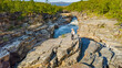 © AmazingAerialAgency - Aerial view of a scenic canyon with a woman walking along the abiskojakka river surrounded by beautiful rocks and lush nature, Abisko National Park, Sweden.