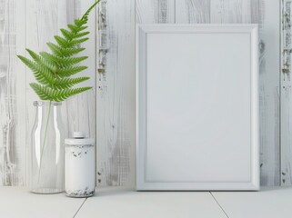 A blank white frame sits on a white table with a white wood wall background A fern branch is in a glass jar with a white vase behind it