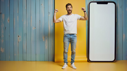 A cheerful young man celebrates in front of a large smartphone display, showcasing excitement and positivity. This image is perfect for tech promotions, social media campaigns, or lifestyle branding