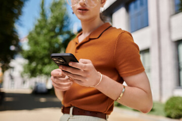 An individual engages with their smartphone while surrounded by greenery and modern architecture.