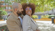 © Krakenimages.com - An interracial couple smiles joyfully in a sunny urban park setting, capturing the essence of love and togetherness in the city.