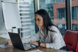 © sashafolly - Serious Asian businesswoman in glasses and white shirt works on laptop staying late in office