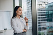 © sashafolly - Young businesswoman stands by office window gazing thoughtfully at city skyline